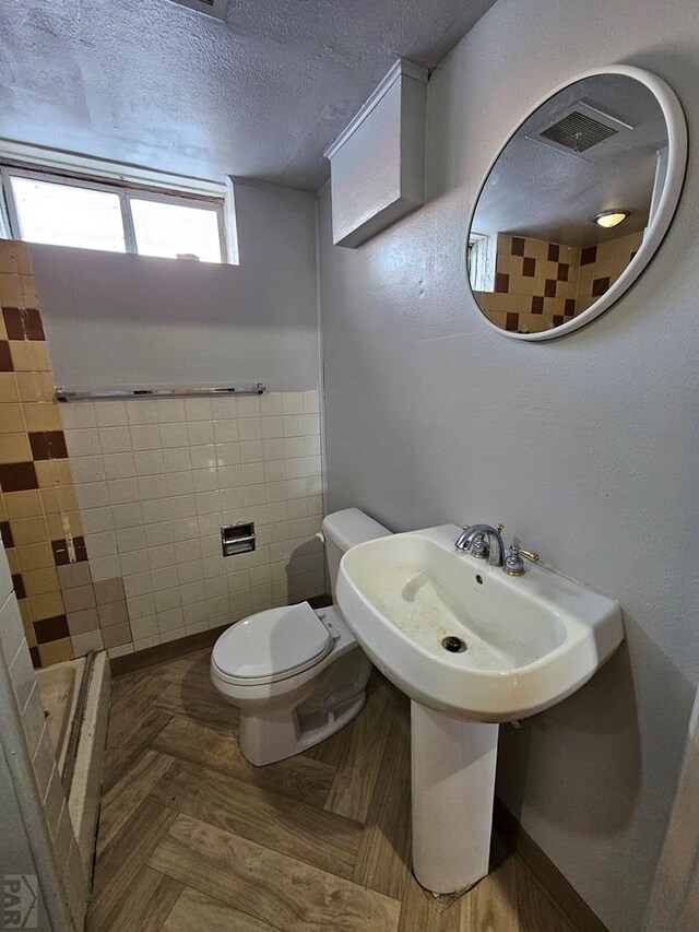 half bathroom with toilet, tile walls, visible vents, and a textured ceiling