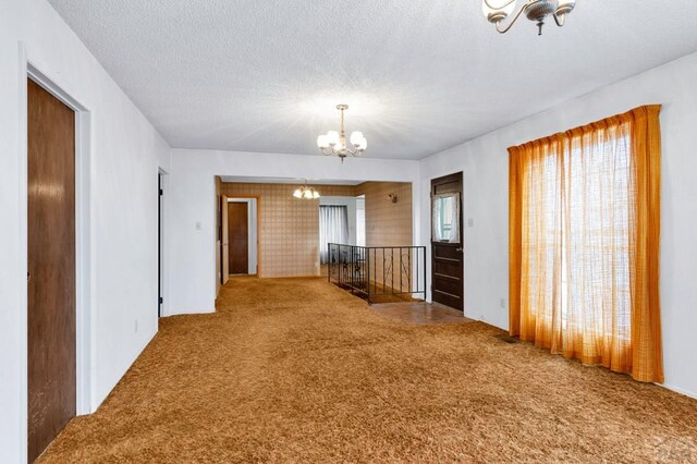 carpeted empty room featuring a healthy amount of sunlight, a textured ceiling, and an inviting chandelier