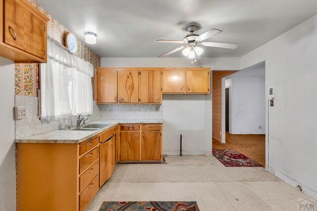 kitchen with ceiling fan, a sink, light countertops, backsplash, and brown cabinetry