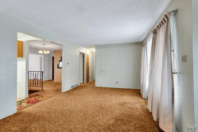 spare room featuring visible vents, light carpet, a textured ceiling, and an inviting chandelier