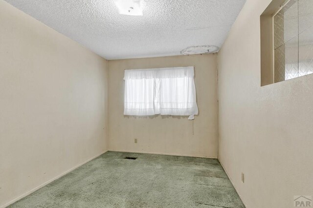 spare room featuring baseboards, light colored carpet, visible vents, and a textured ceiling