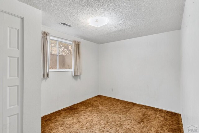 spare room with carpet floors, visible vents, and a textured ceiling