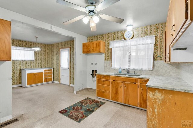 kitchen featuring baseboards, light countertops, a sink, and wallpapered walls