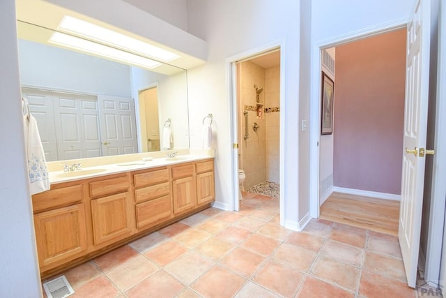 bathroom with tiled shower, double vanity, toilet, tile patterned flooring, and baseboards