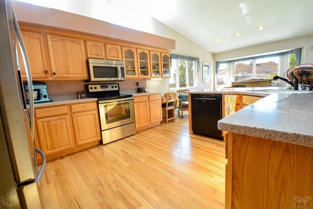kitchen featuring stainless steel appliances, a sink, lofted ceiling, light wood-type flooring, and light countertops