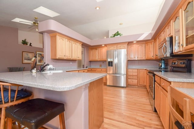 kitchen with stainless steel appliances, a peninsula, a kitchen breakfast bar, light wood finished floors, and a skylight