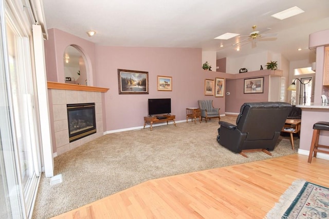 carpeted living room featuring a fireplace, wood finished floors, vaulted ceiling, ceiling fan, and baseboards