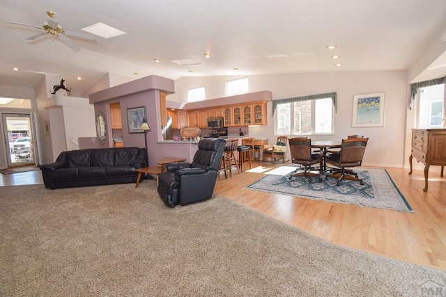 living area with lofted ceiling, light wood-type flooring, baseboards, and ceiling fan