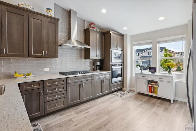 16840 New Autum Dr, Monument, CO 80132 - kitchen with wall chimney range hood, stainless steel appliances, backsplash, dark brown cabinetry, and light wood-style flooring
