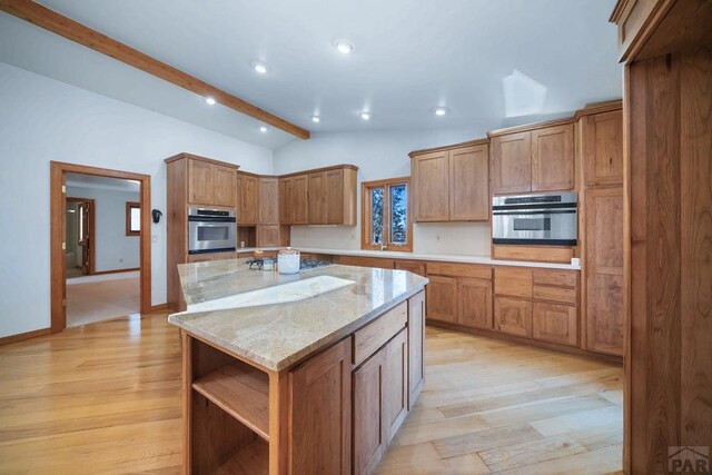 kitchen featuring lofted ceiling with beams, light stone counters, light wood-style flooring, stainless steel appliances, and a sink