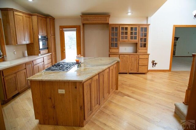 kitchen with light wood finished floors, glass insert cabinets, stainless steel appliances, and brown cabinetry