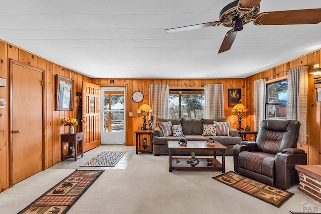 living area with a ceiling fan, light carpet, and wooden walls