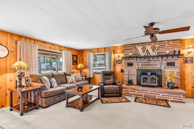 carpeted living area with ceiling fan, wood walls, a wood stove, and a healthy amount of sunlight