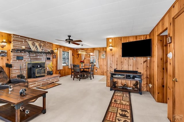 living area featuring wooden walls, a ceiling fan, a wood stove, and light colored carpet