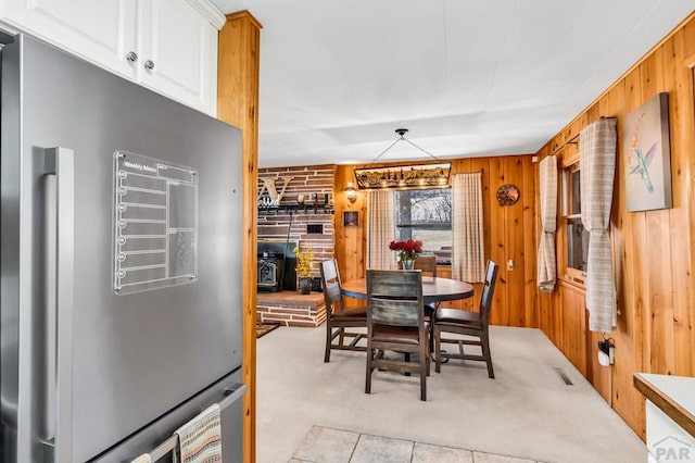 dining space featuring a wood stove, light carpet, wood walls, and visible vents