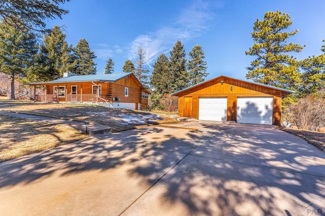 view of front of home featuring covered porch, an outbuilding, log siding, and a detached garage