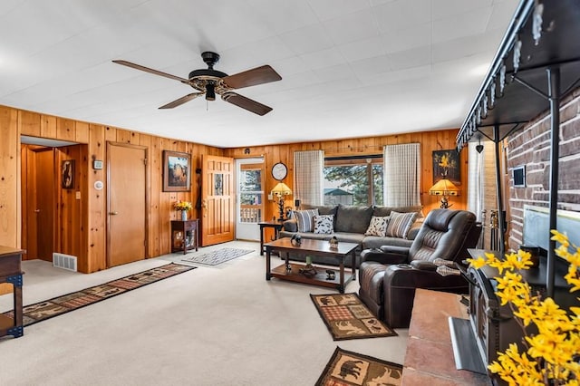 living area with carpet floors, visible vents, ceiling fan, and wooden walls