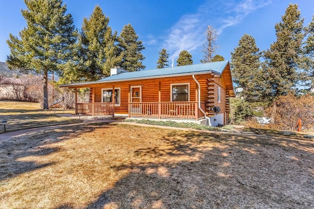 cabin with metal roof, a porch, log exterior, a front lawn, and a chimney