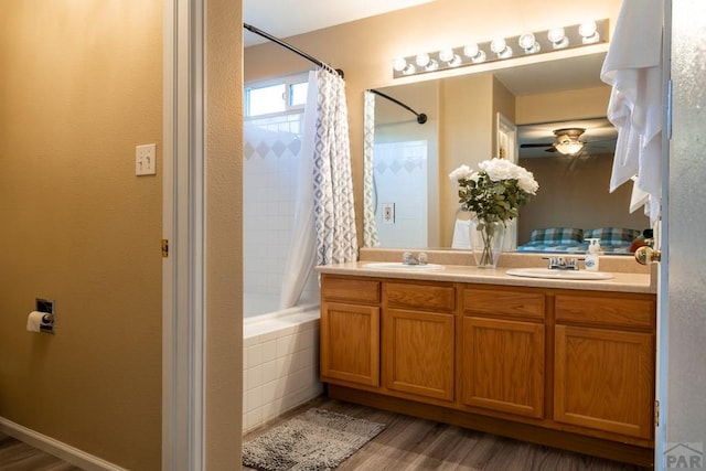 full bathroom featuring wood finished floors, double vanity, ceiling fan, a sink, and tiled shower / bath