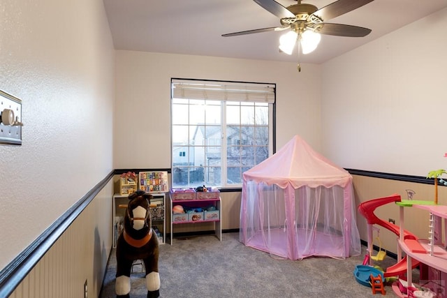 recreation room featuring carpet, wainscoting, and ceiling fan