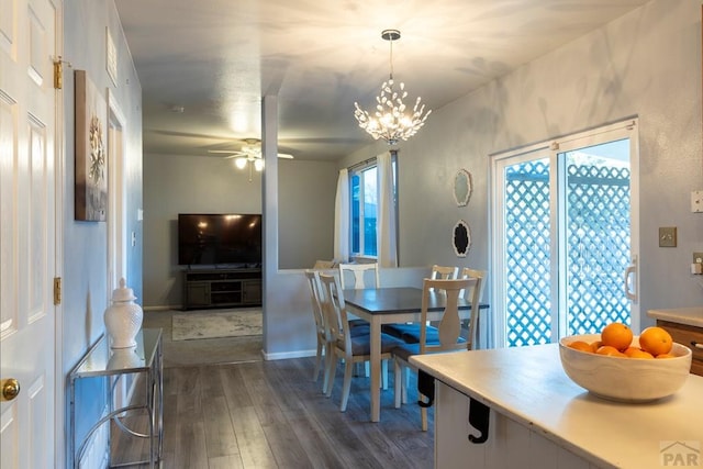 dining area featuring ceiling fan with notable chandelier, dark wood-style floors, and baseboards