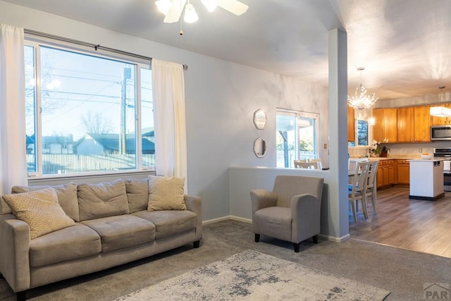 living room featuring carpet flooring, ceiling fan with notable chandelier, and baseboards