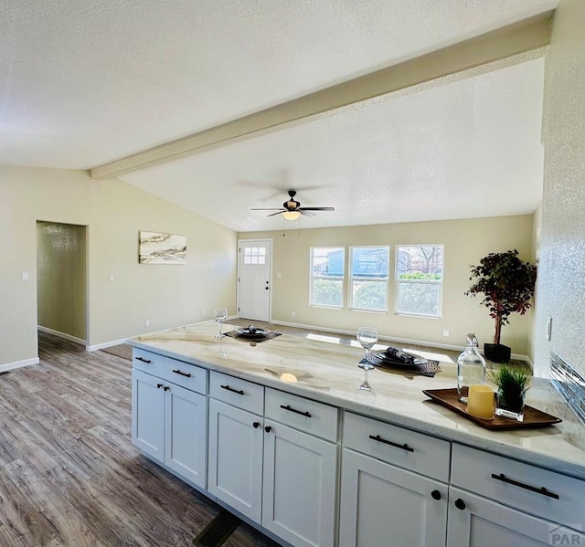 kitchen featuring wood finished floors, open floor plan, vaulted ceiling with beams, and light stone countertops