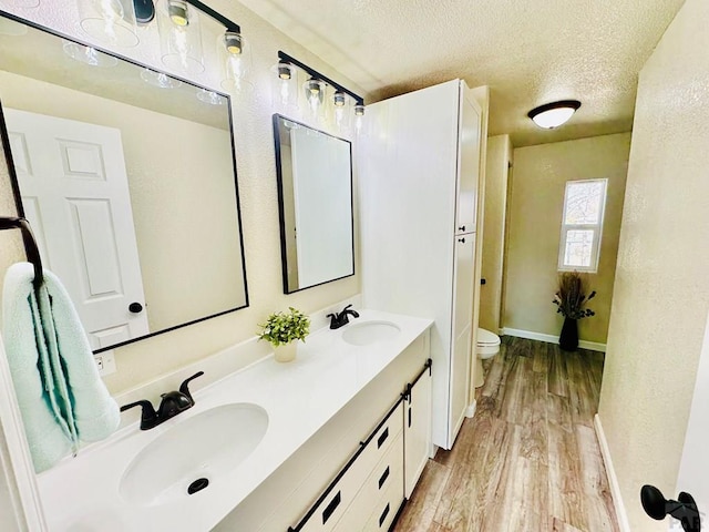 bathroom featuring toilet, a textured ceiling, a sink, and wood finished floors