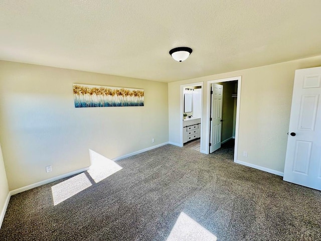 unfurnished bedroom with a textured ceiling, carpet floors, a walk in closet, and baseboards