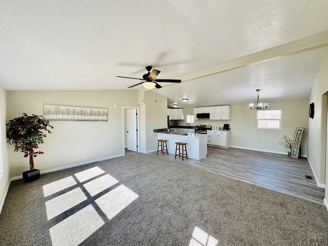 unfurnished living room with lofted ceiling, a textured ceiling, baseboards, and ceiling fan with notable chandelier