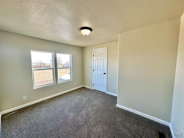 spare room with dark carpet, visible vents, and baseboards