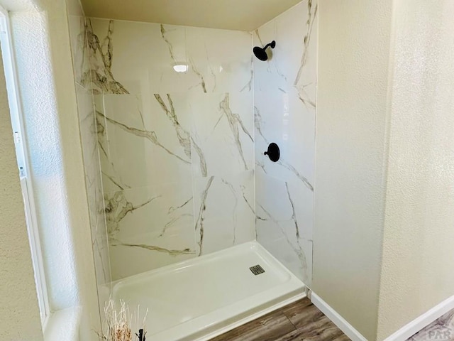 bathroom featuring baseboards, a textured wall, a marble finish shower, and wood finished floors