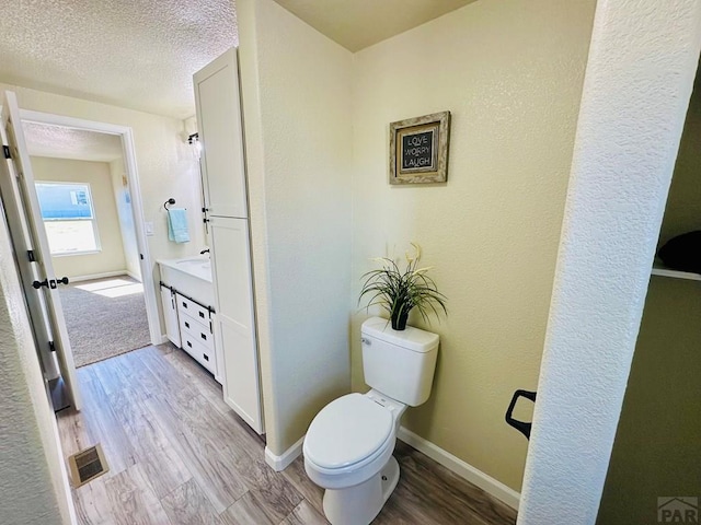 bathroom featuring a textured ceiling, toilet, wood finished floors, visible vents, and vanity