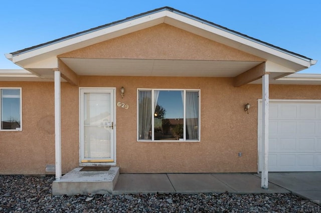 doorway to property featuring an attached garage and stucco siding