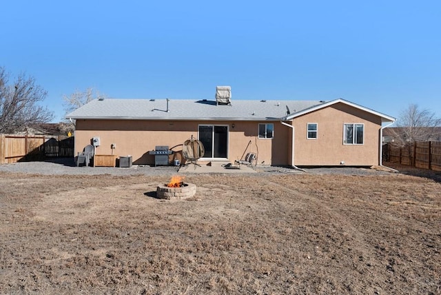 rear view of property featuring fence, a fire pit, and stucco siding