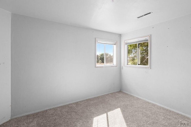 empty room with carpet, visible vents, and baseboards