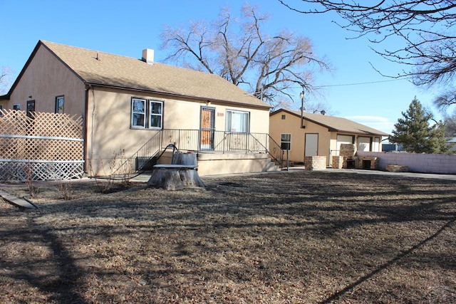 back of property with a shingled roof, fence, a chimney, and stucco siding