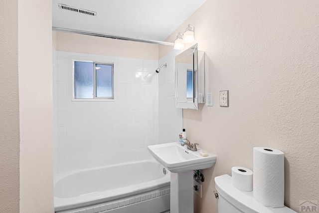 bathroom featuring toilet, a textured wall, shower / washtub combination, and visible vents