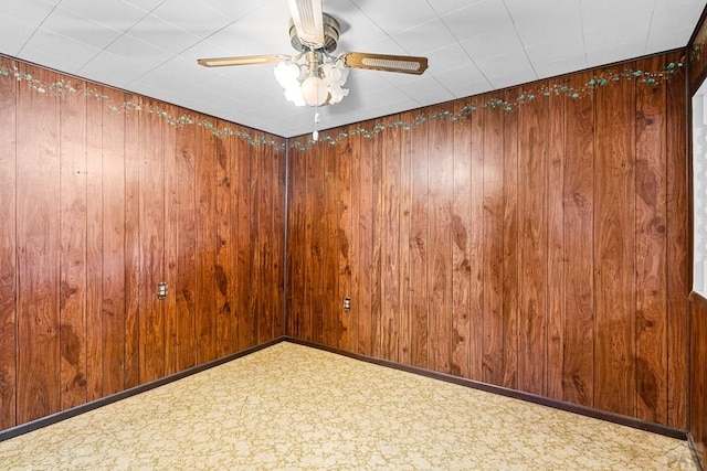 spare room featuring wood walls, a ceiling fan, and baseboards