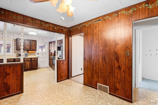 kitchen featuring light floors, wooden walls, visible vents, and a ceiling fan