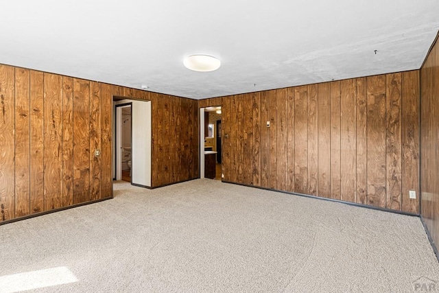 spare room featuring carpet floors, wood walls, and baseboards