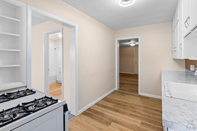 kitchen with white gas stove, a sink, baseboards, white cabinets, and light wood finished floors