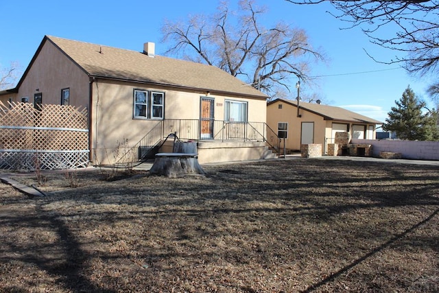 back of house featuring stucco siding, a chimney, fence, and roof with shingles