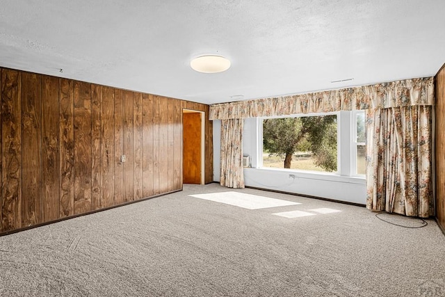 unfurnished room with carpet, wood walls, and a textured ceiling