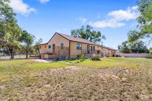 back of house with stucco siding, fence, and a yard