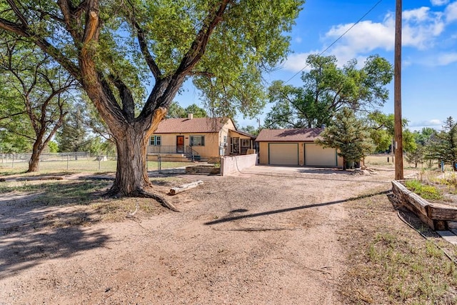 single story home featuring an outbuilding, a garage, fence, dirt driveway, and stucco siding