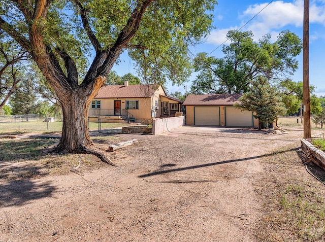 single story home featuring a garage, dirt driveway, fence, an outdoor structure, and stucco siding