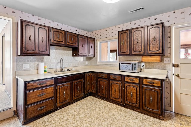 kitchen with a sink, visible vents, light countertops, stainless steel microwave, and wallpapered walls