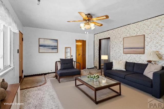 living area with a ceiling fan and wallpapered walls