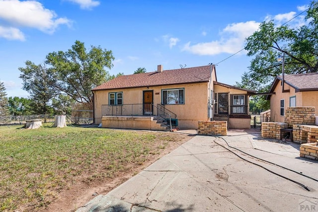 view of front of house featuring a chimney, stucco siding, a sunroom, fence, and a front lawn